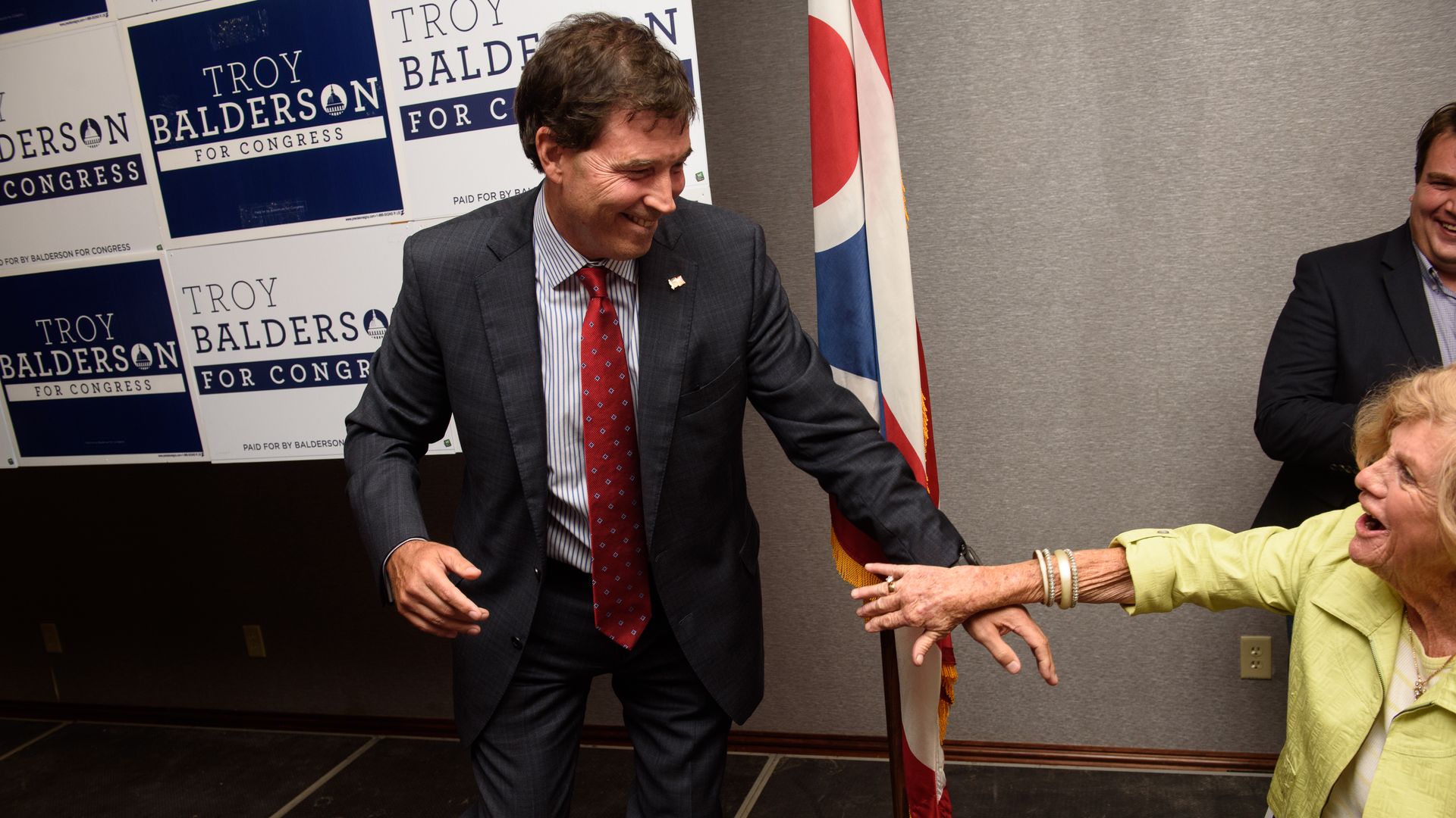 Republican Troy Balderson stepping down off a platform after giving a speech and smiling at a member in the crowd who is reaching out a hand toward him