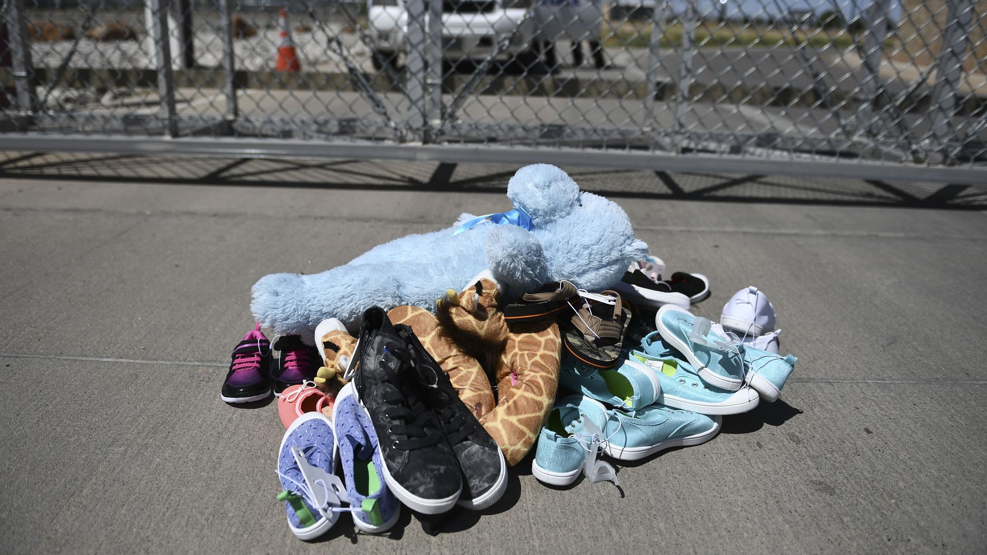 A pile of children's shoes and toys in front of a chain link fence at the border