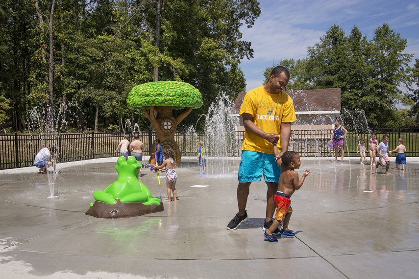 a couple of kids stand under a tree splash pad 