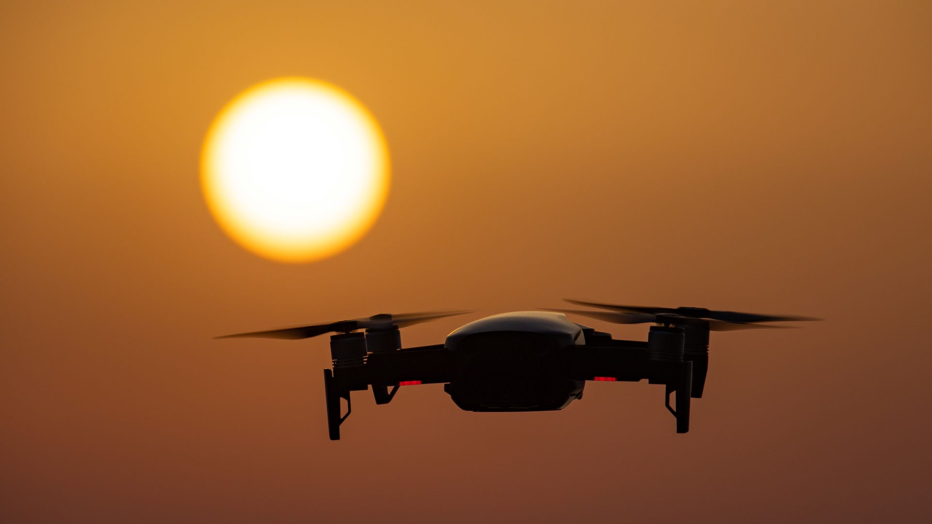 A DJI drone is seen hovering in front of a setting sun.