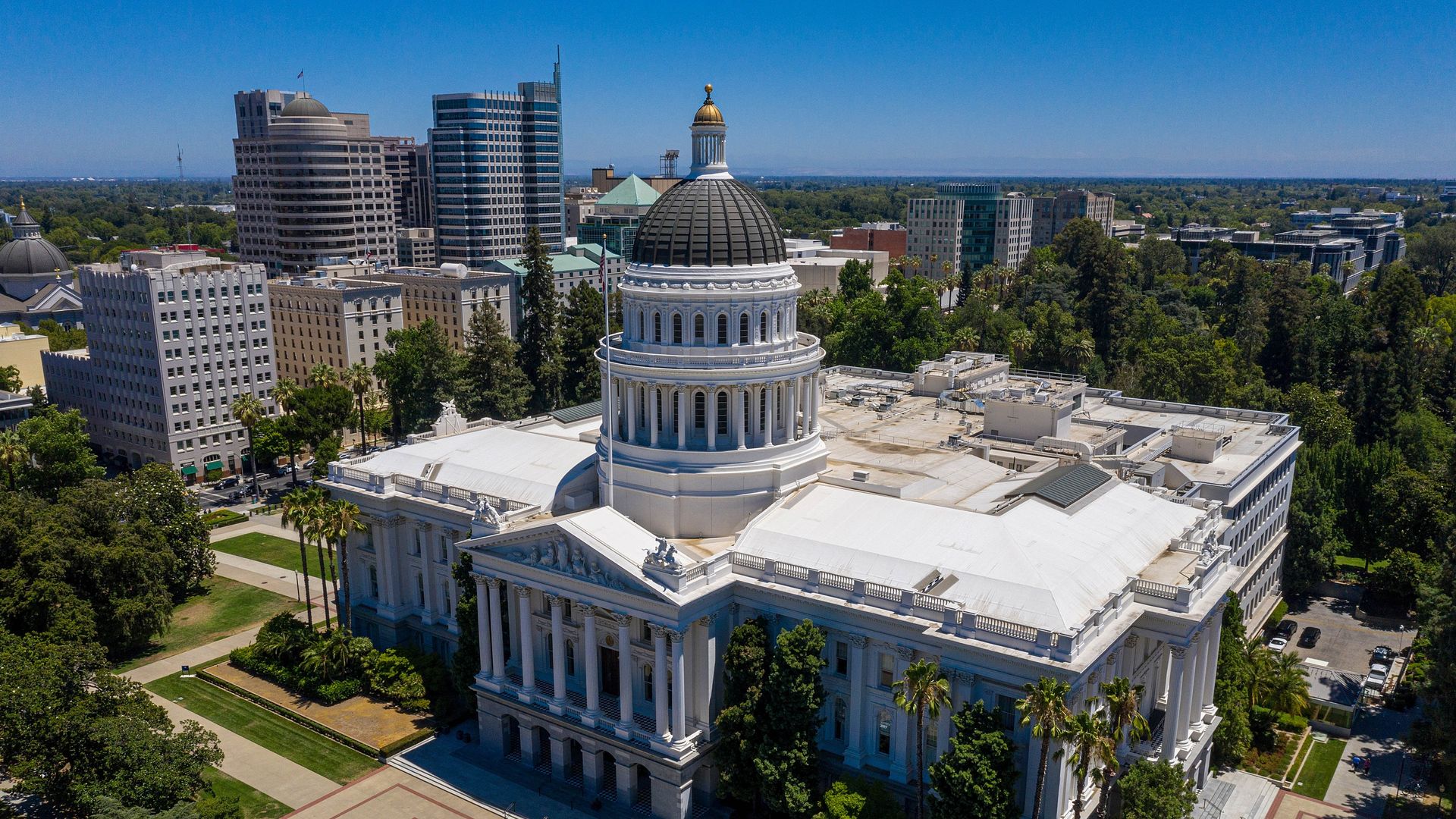 Aerial photo of the California state capitol building, with some high rises and trees behind it.
