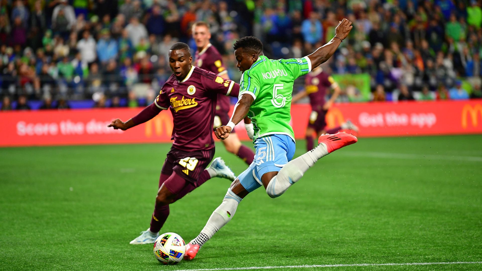 A soccer player in green is captured leaping with his left leg poised to kick. 