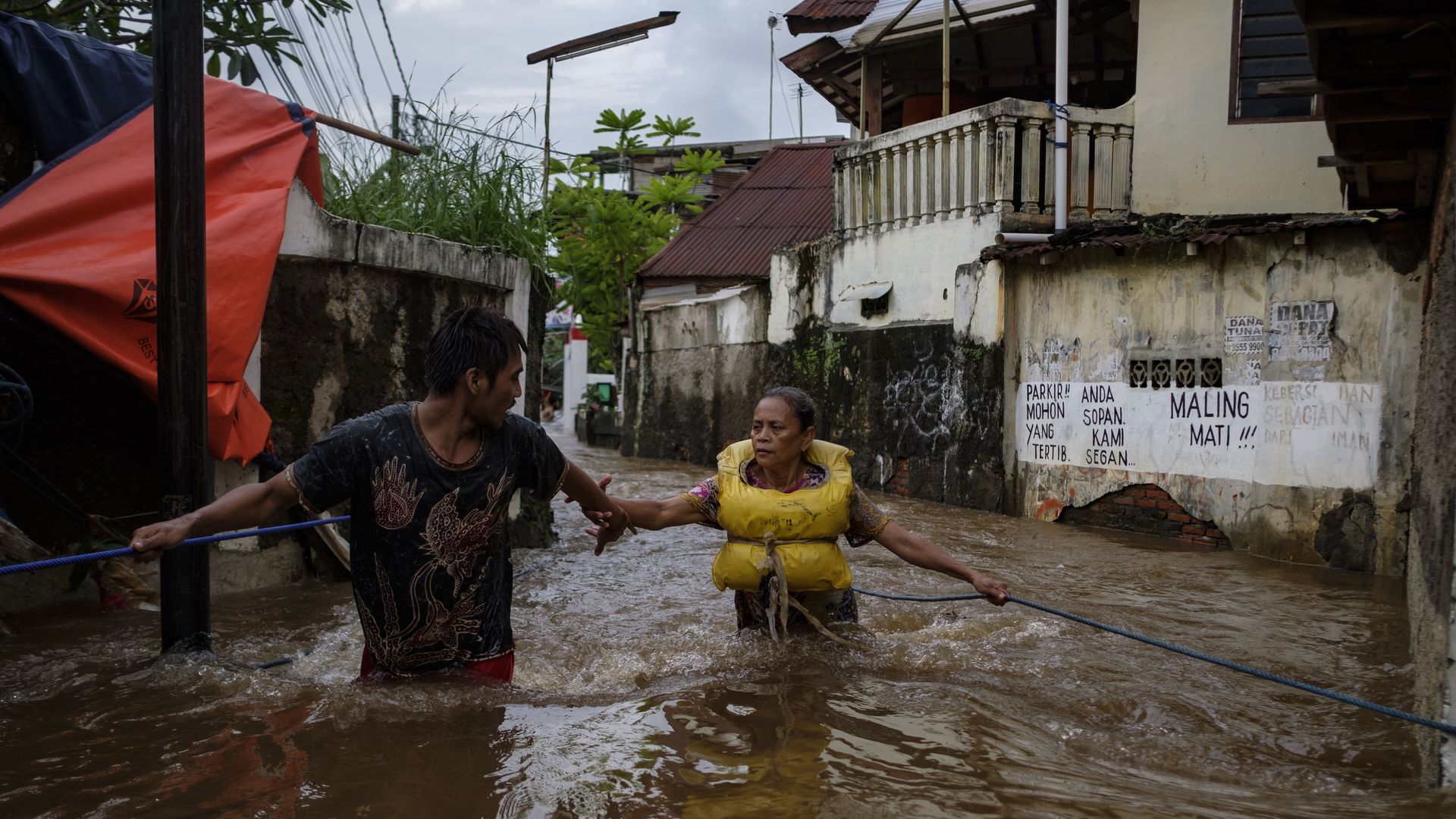 An Indonesian man helps a woman navigate a heavy current in a flooded neighborhood on February 20, 2021 in Jakarta, Indonesia.