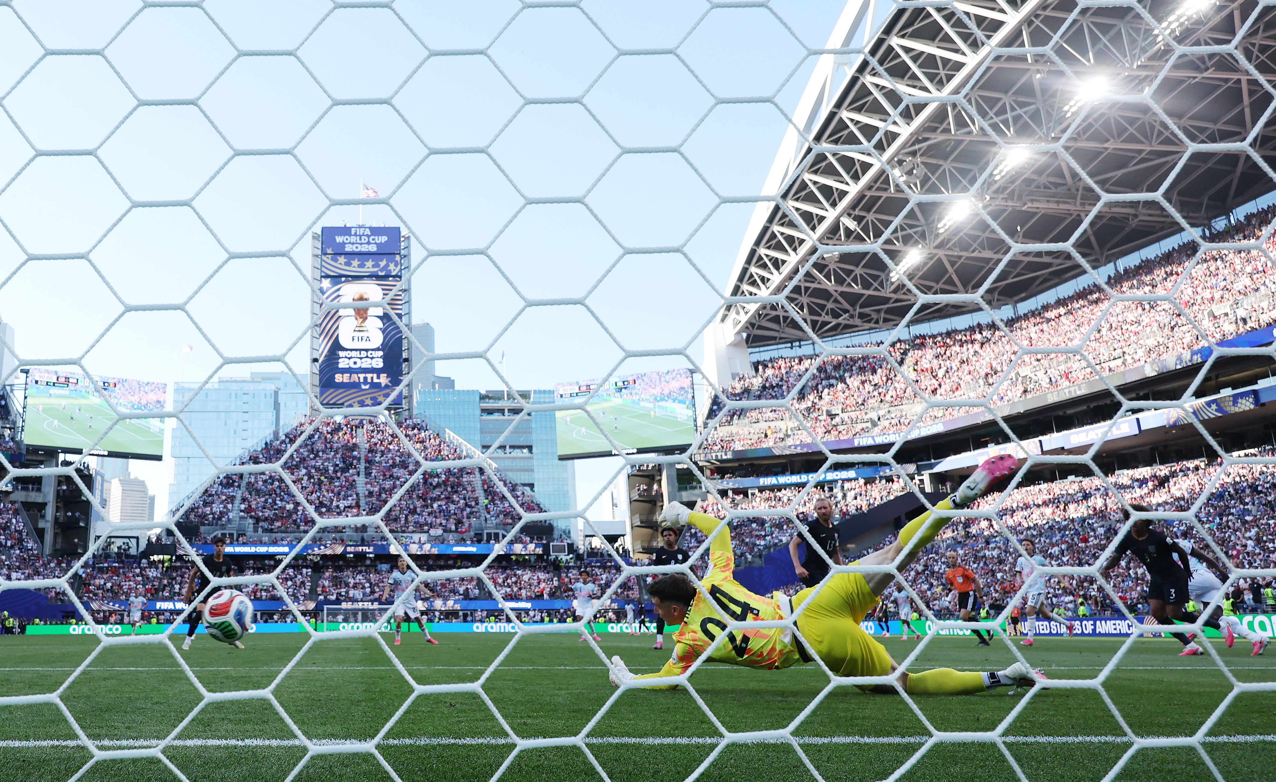 View from behind the goal as U.S. goalkeeper Matt Freese dives unsuccessfully for a shot that crosses the line, with Belgium players and a packed crowd at Seattle's stadium in the background.