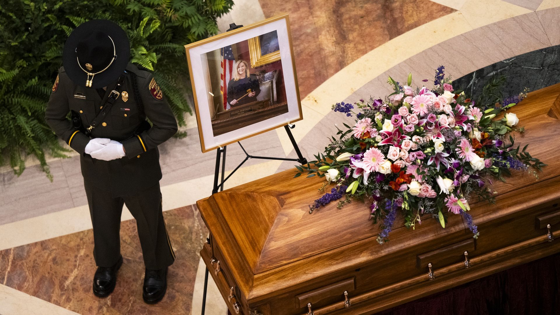 A state trooper stands next to a portrait of Melissa Hortman accompanying her casket in the state Capitol.