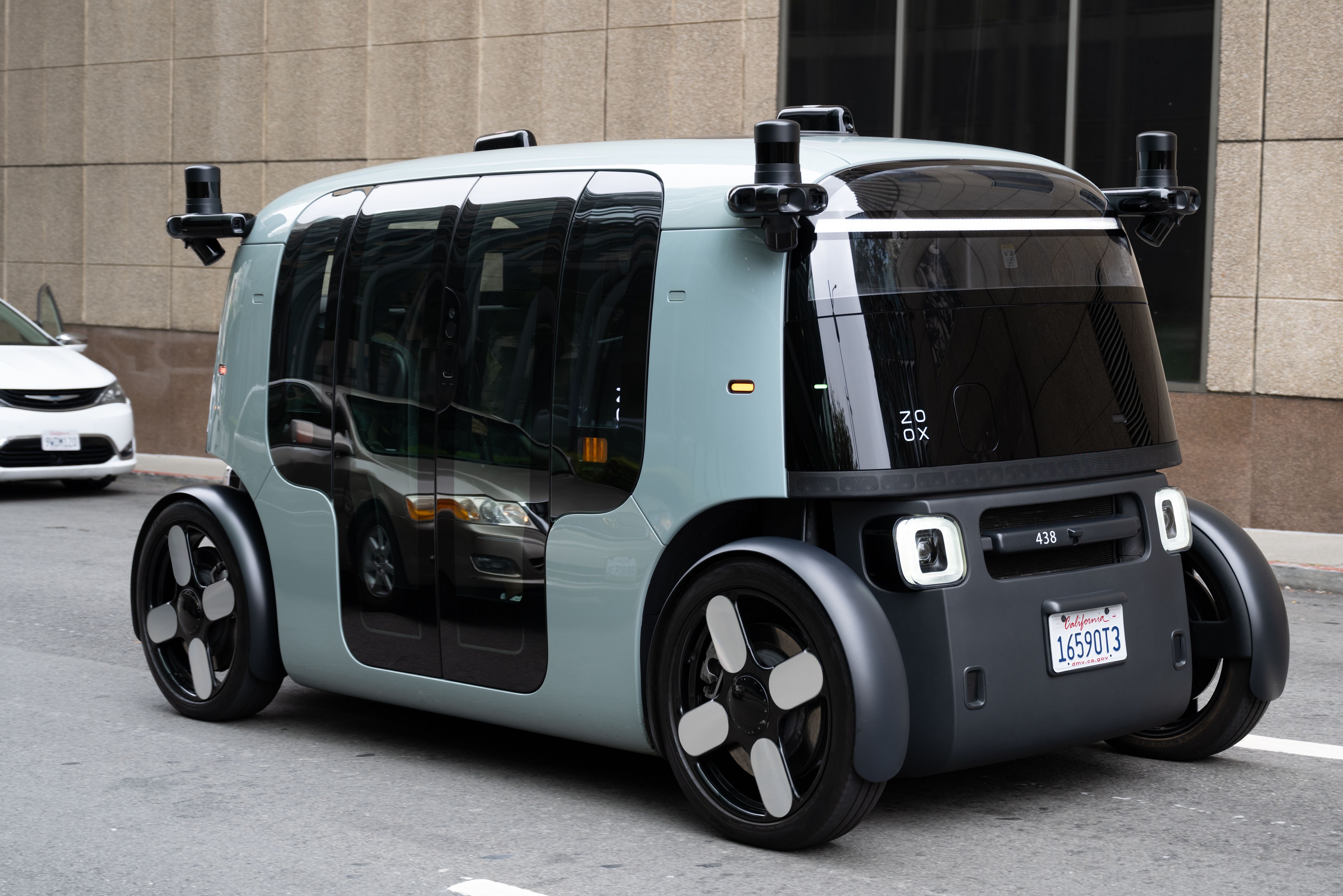 Photo of a blue-gray and black robotaxi with Zoox label. 