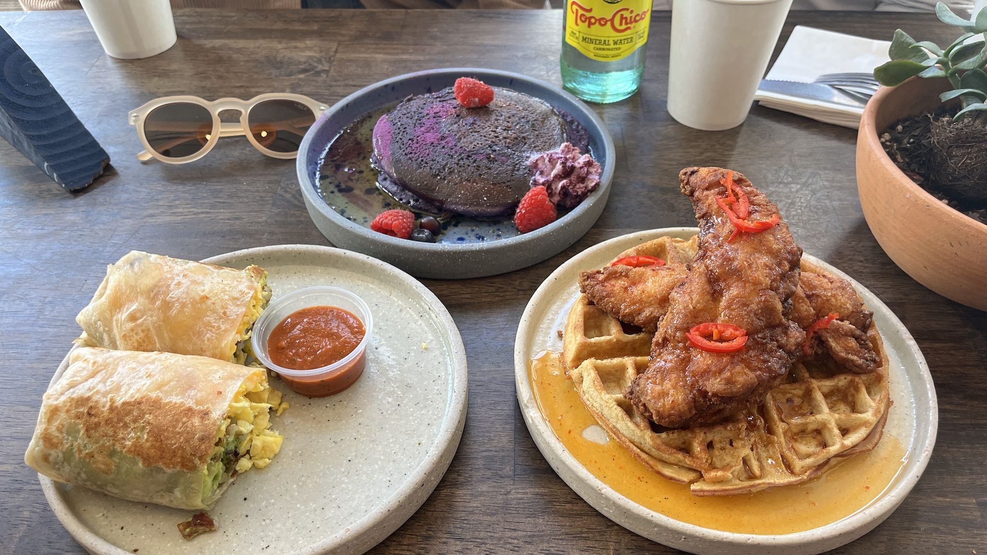 A breakfast burrito, purple pancakes and chicken and waffles on a table at a restaurant.