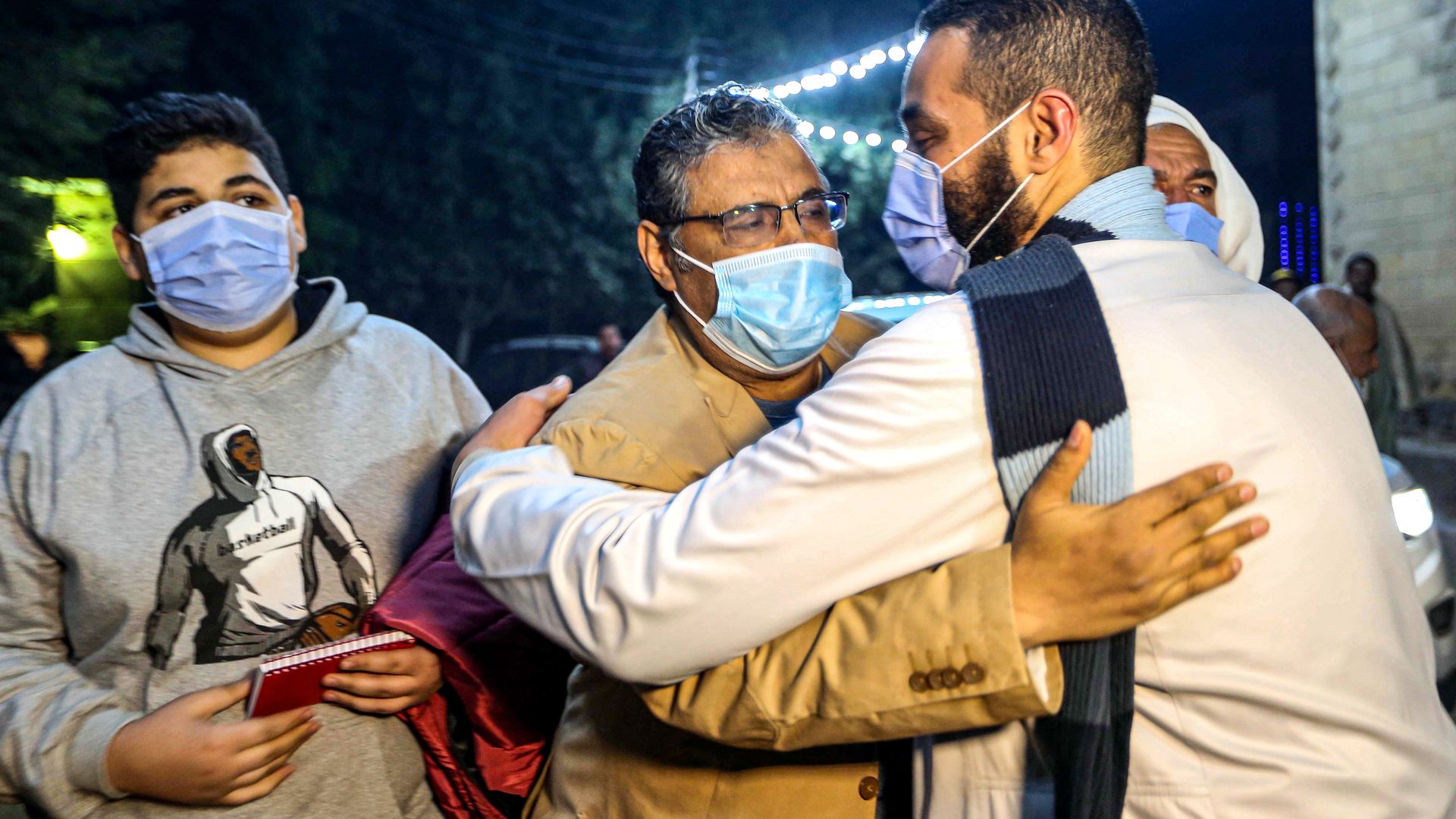 Mahmoud Hussein (C), an Egyptian national and senior journalist for Qatar-based Al Jazeera Arabic, is embraced by a man upon his arrival at his family home in the Giza village of Zawyet Abu Musallam