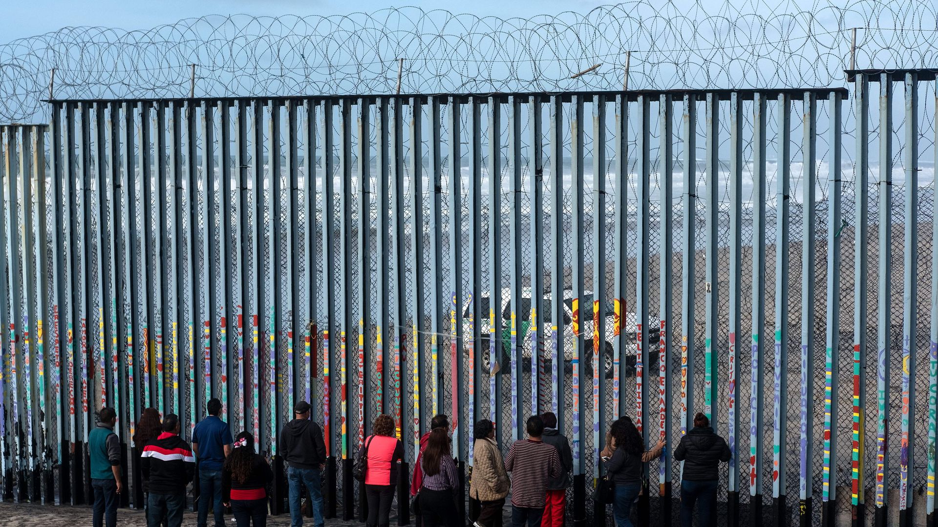People look at US border patrol guards through the US-Mexico border fence.