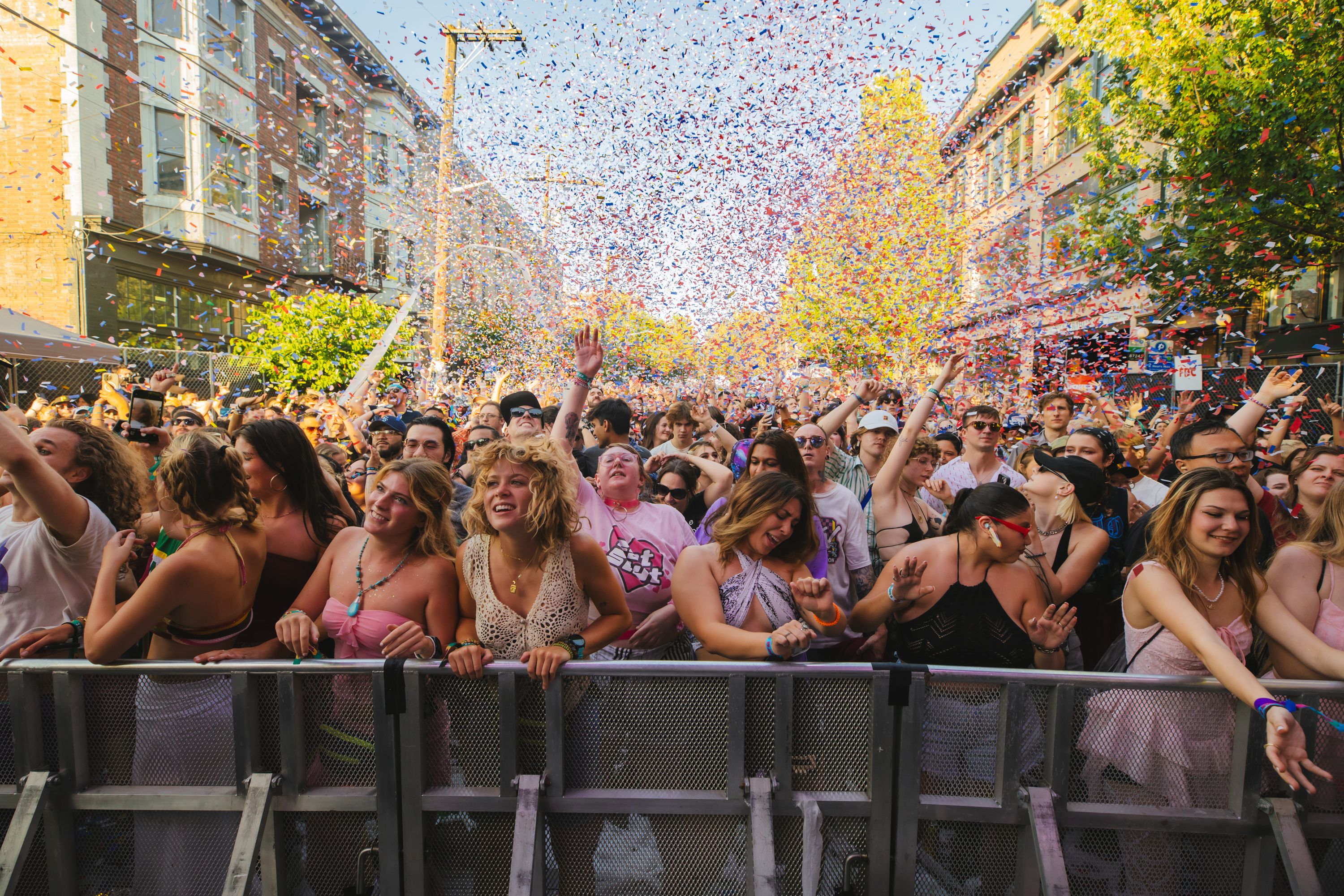 People stand in front of a barrier watching a concert, facing the stage, which isn't shown, as confetti bursts in the air behind them.