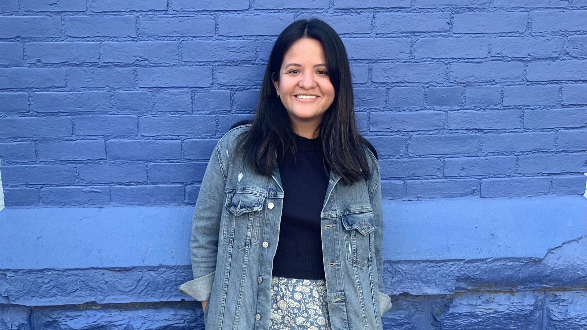 Maria Hurtado poses in front of a blue brick wall