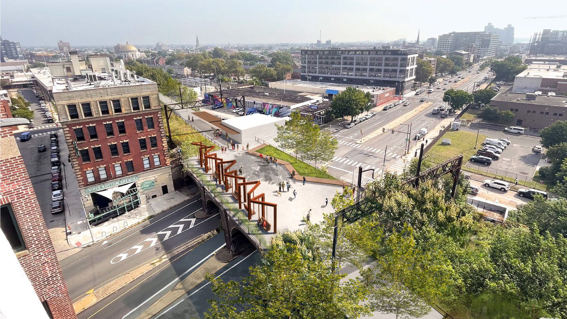 Aerial view of a city street with historic buildings, parked cars, and a pedestrian plaza with geometric sculptures and greenery, surrounded by trees and urban structures.