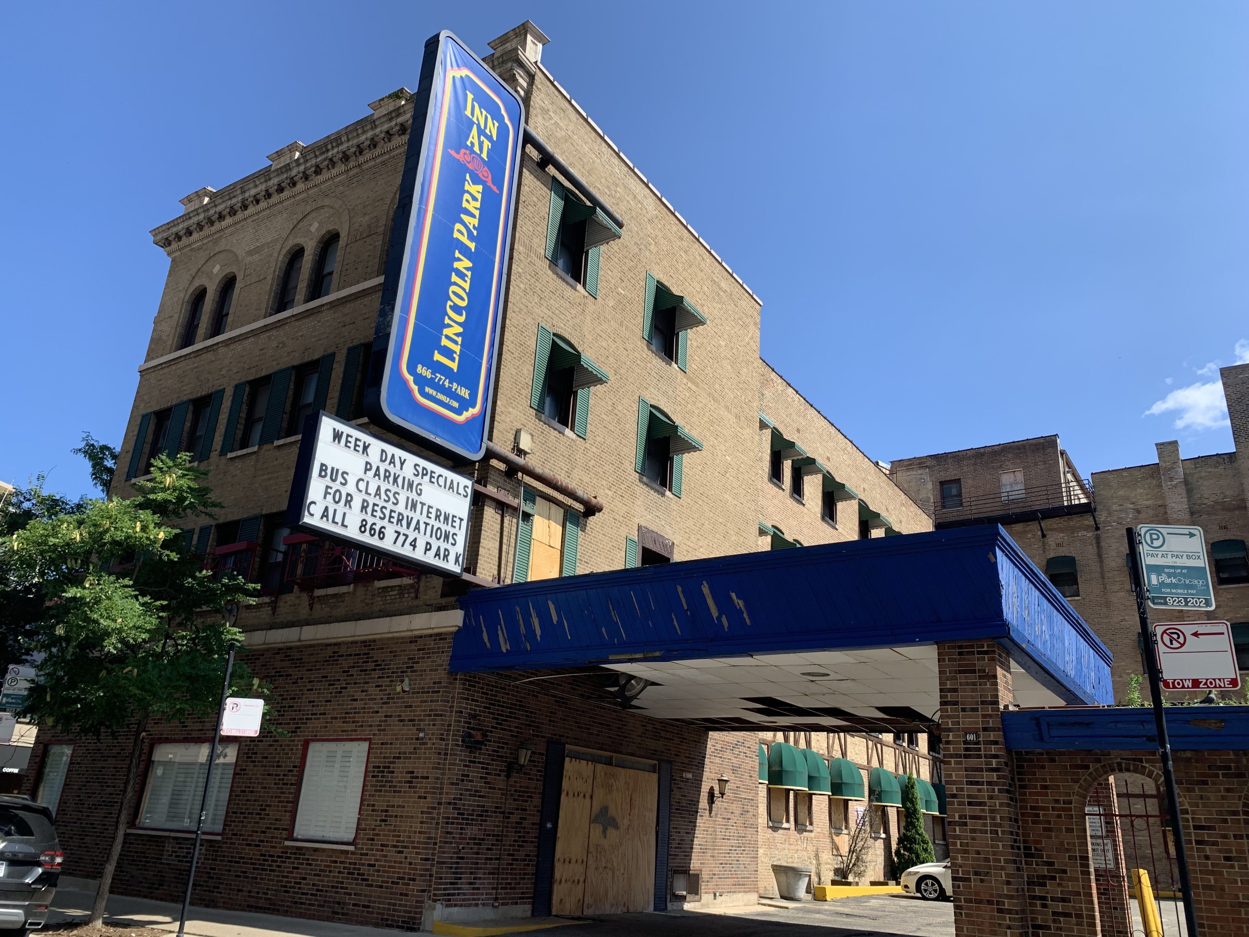 Boarded up hotel with blue covered carport and blue marquee reading Lincoln Park Inn.