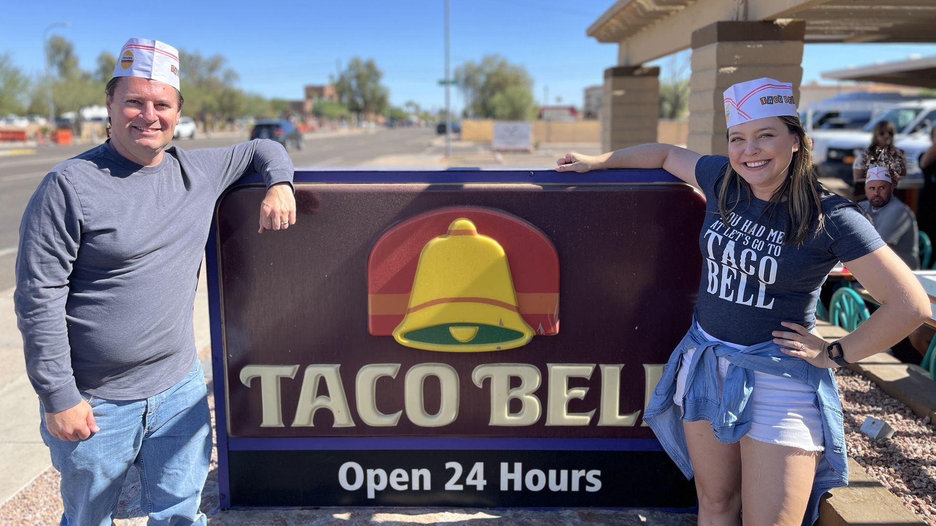 Jeremy Duda and Jessica Boehm smile while posing next to a Taco Bell sign.