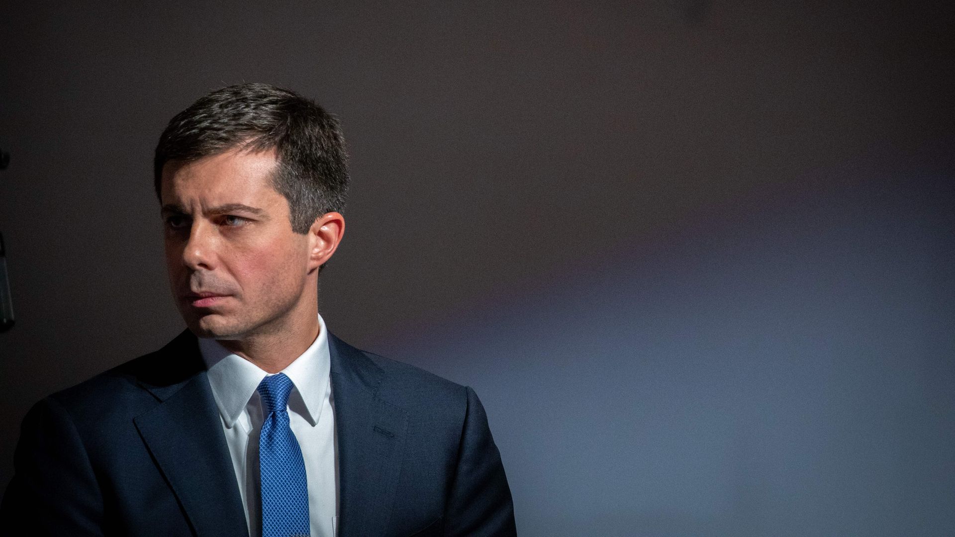 In this image, Buttigieg stands in a suit and tie.