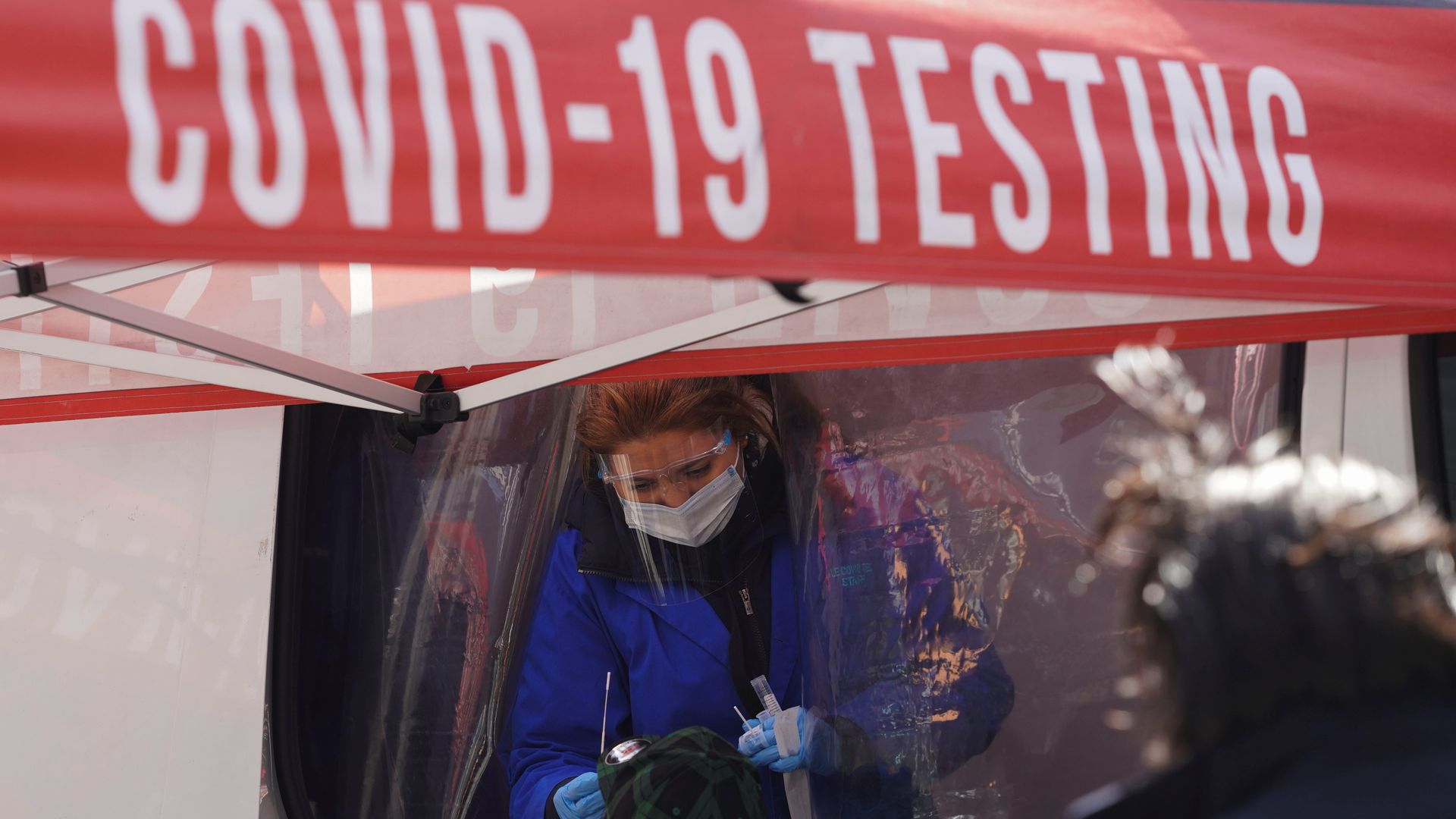 Photo of a worker swabbing a person's nose under a red COVID-19 testing tent
