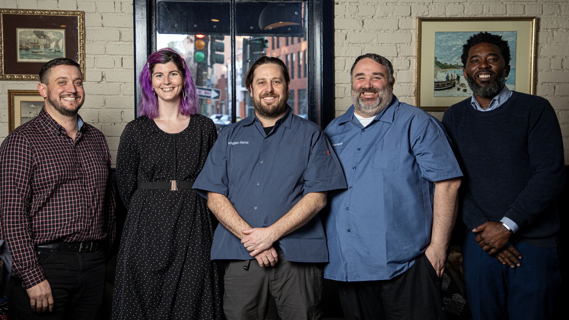 Five people stand in a row in front of a window and smile.