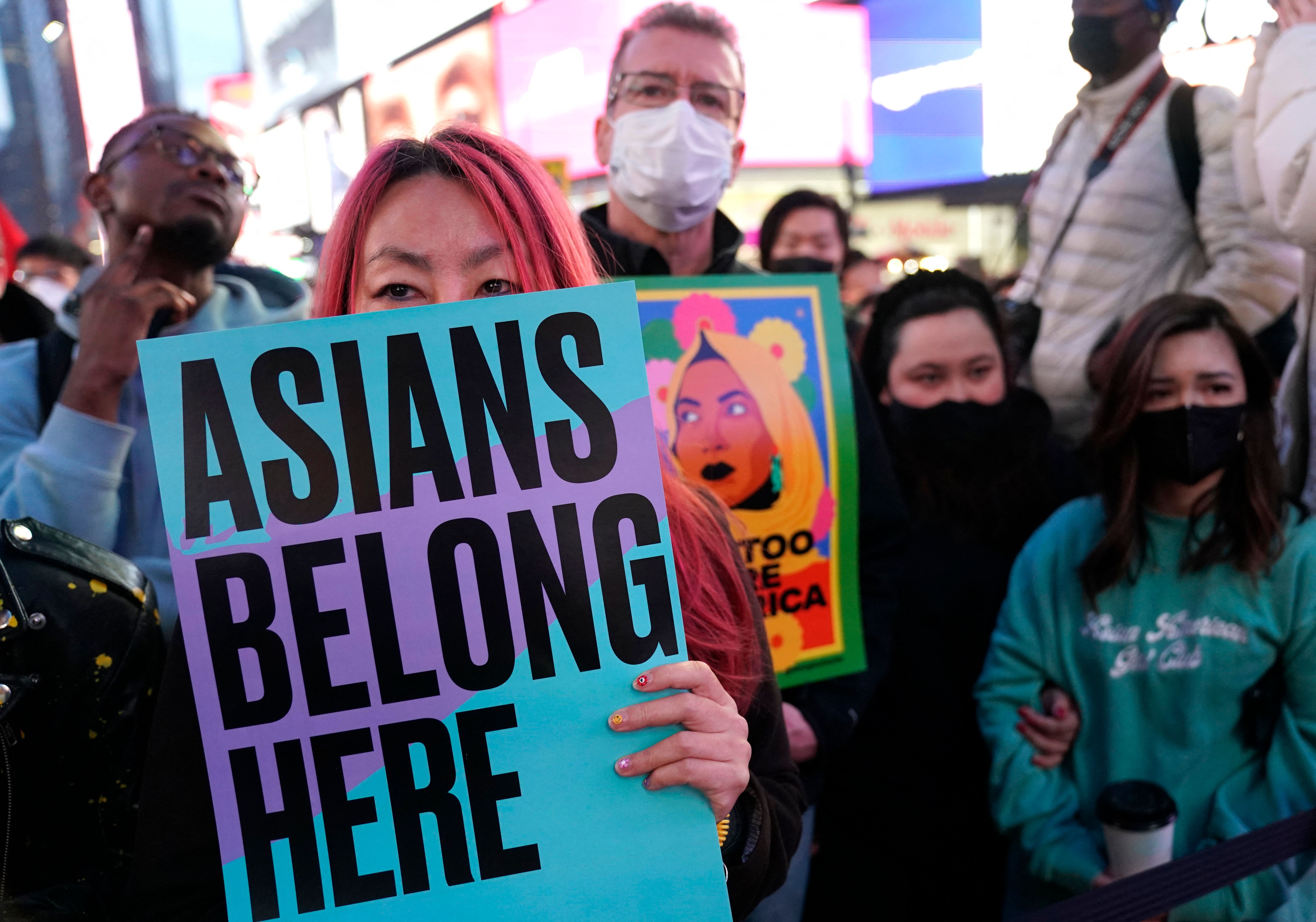 Photo of a person holding a sign that says "Asians belong here," with other people nearby