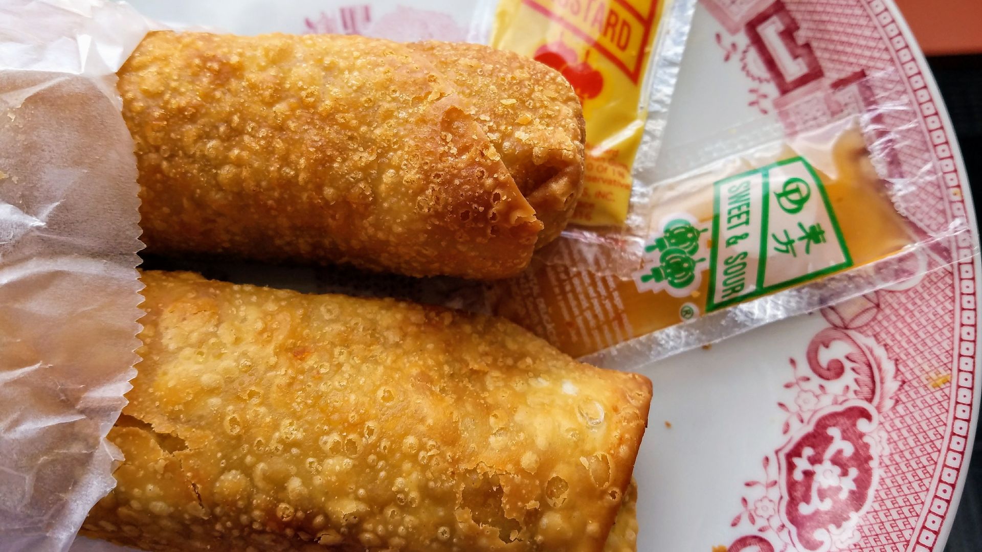 Photo of two egg rolls on a paper plate with a packet of mustard. 