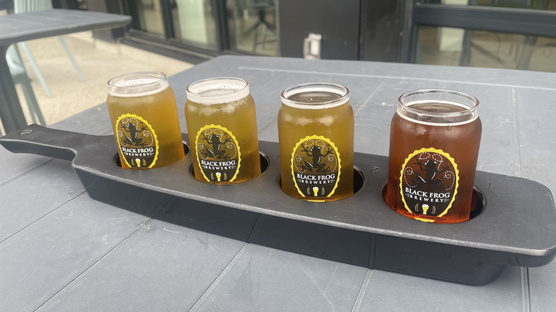 A flight of beers with a "Black Frog" logo on each of the glasses