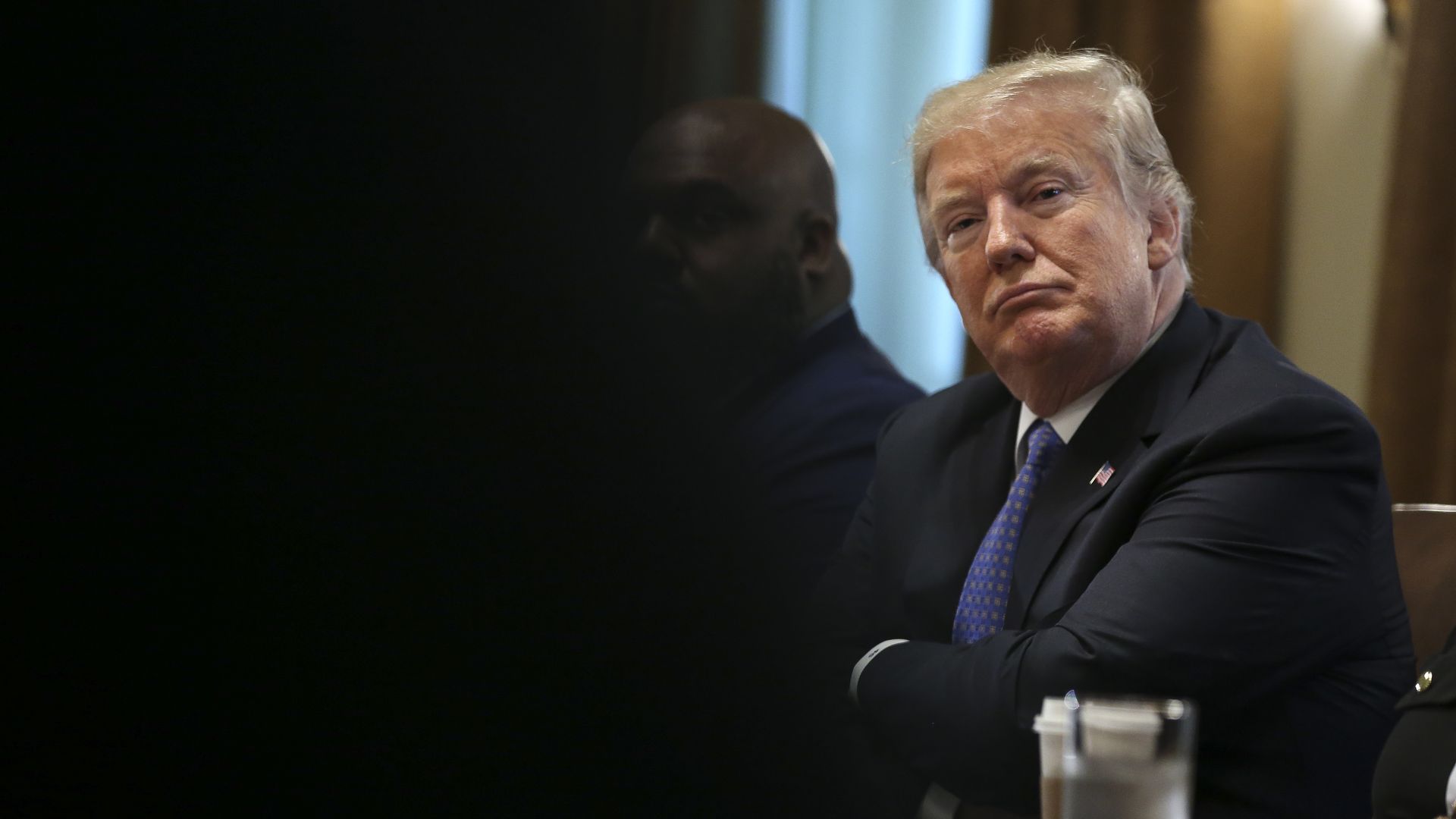 Donald Trump folds his arms across his chest and has a smug, yet happy look on his face as he listens to someone in a meeting