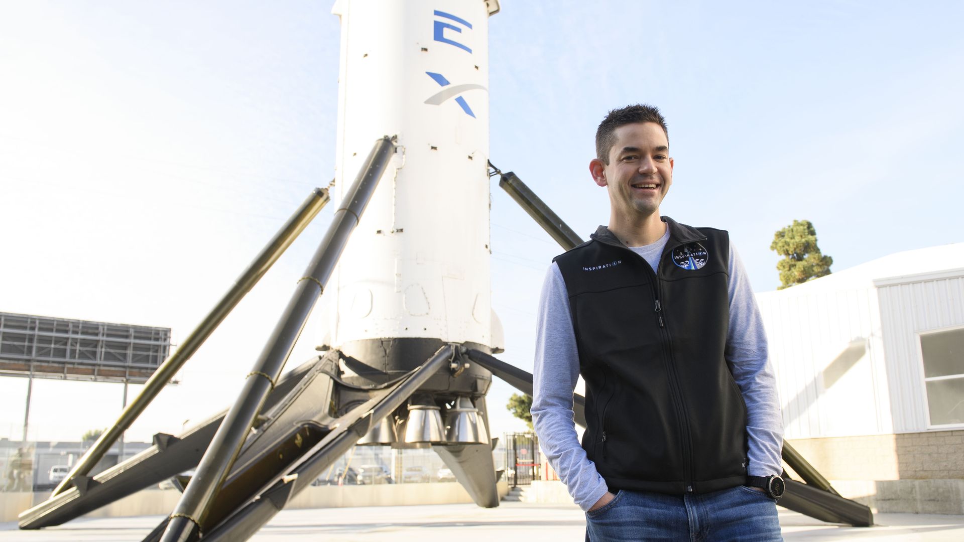 Jared Isaacman stands next to a SpaceX rocket display.