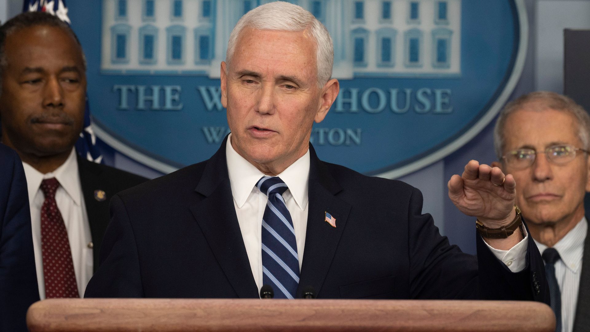 In this image, Pence stands behind a podium in the White House briefing room while wearing a suit
