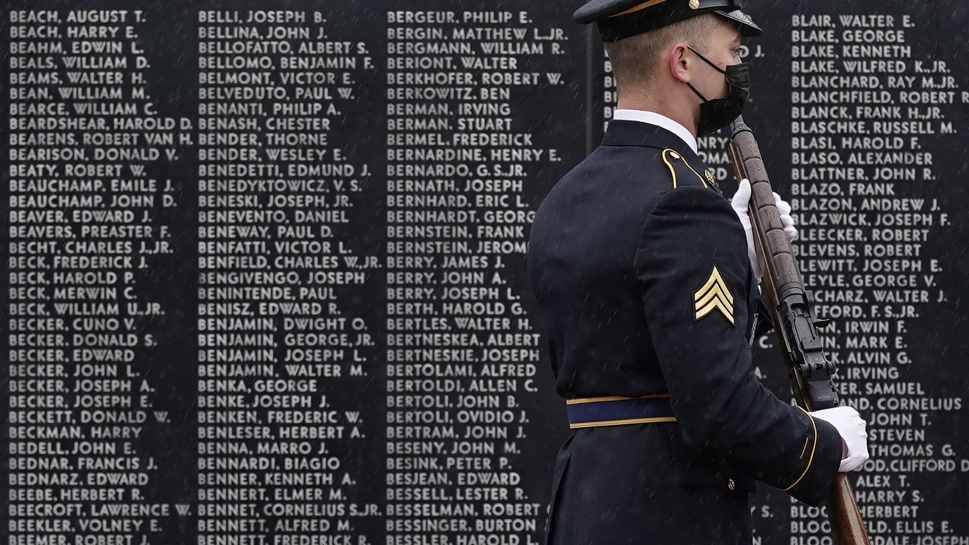 A soldier in uniform walks past long rows of names inscribed on marble