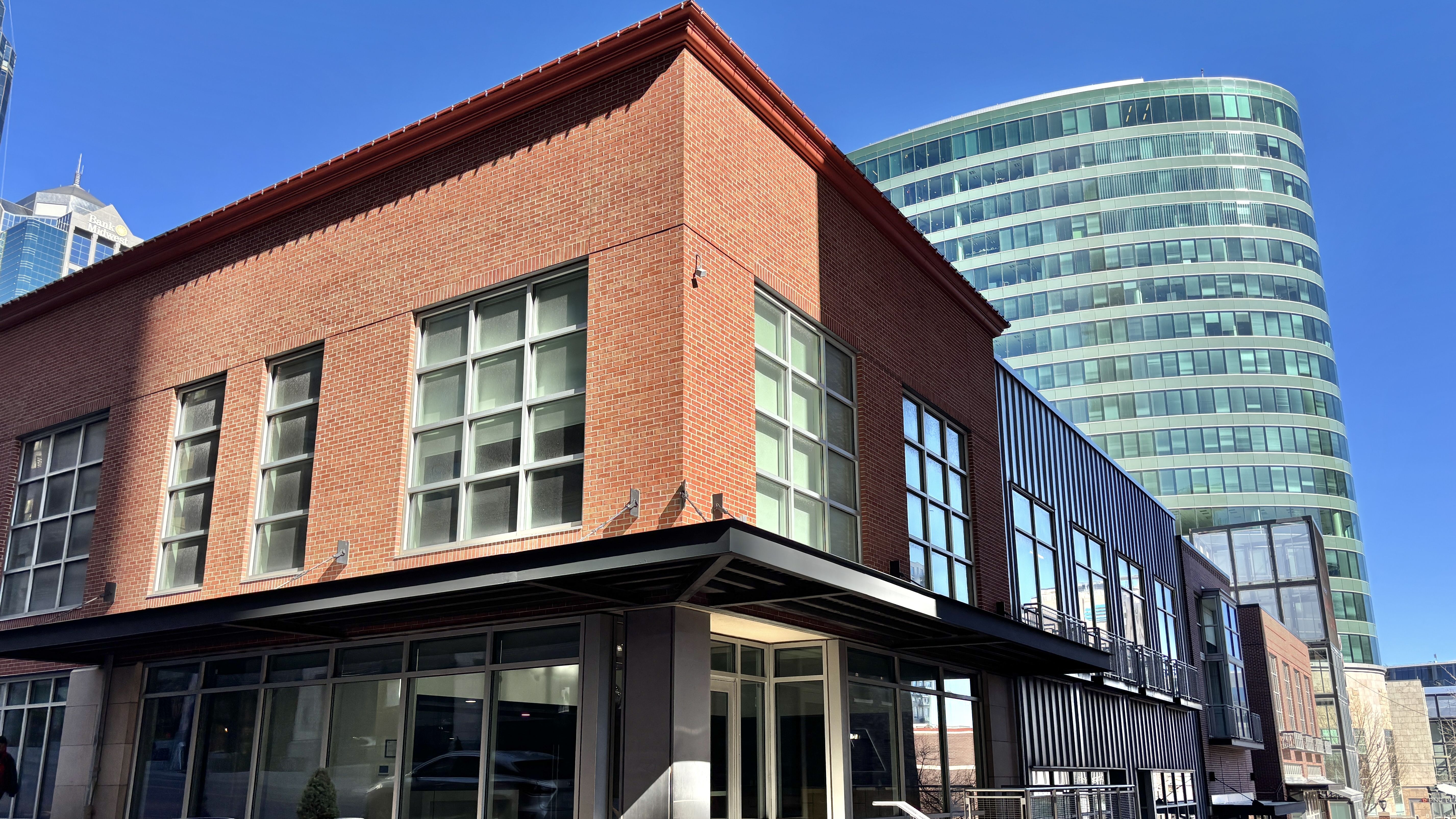A red brick building with large windows and a black metal awning, looking northeast with the curved glass H&R Block tower in the background.