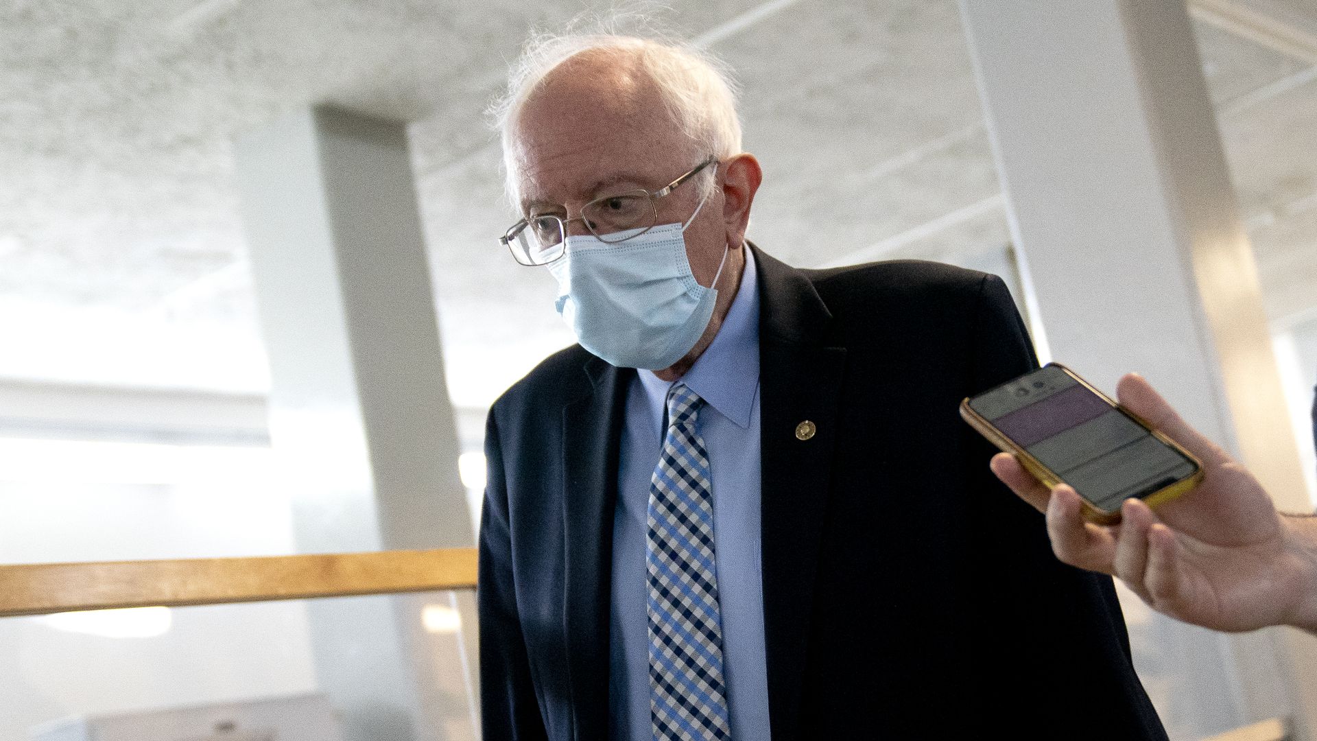 Photo of Bernie Sanders walking with a hand holding a phone extended toward him