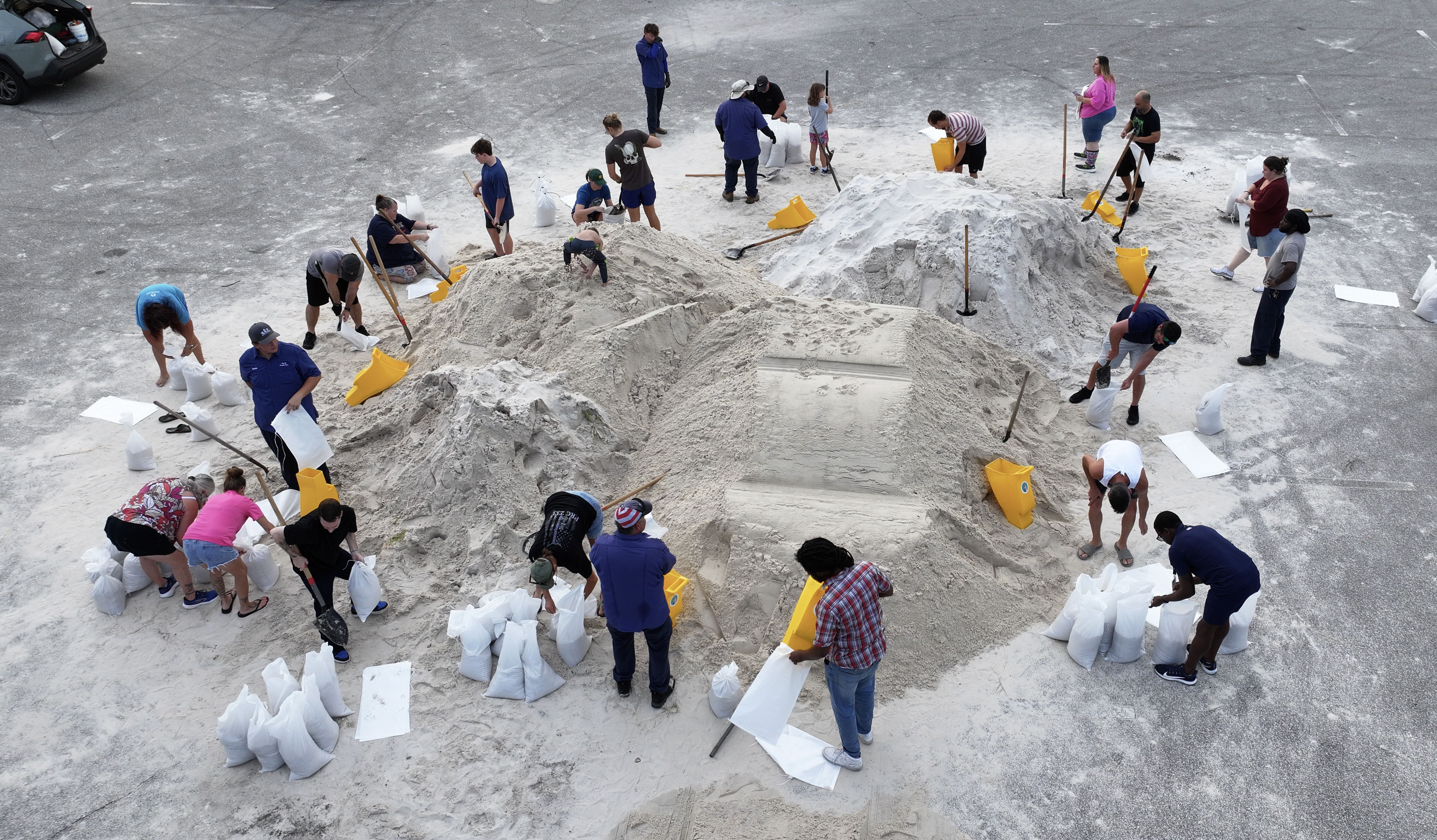 A circle of people around a big mound of sand, filling white sandbags.