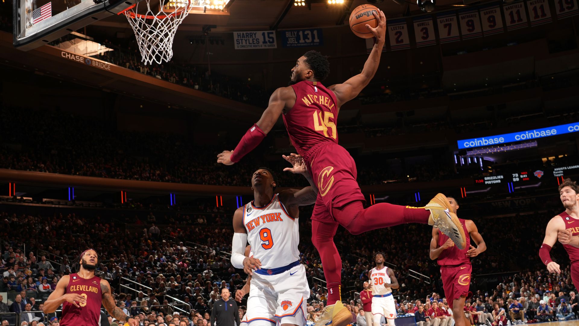 The Cavs' Donovan Mitchell, in red, dunks on the Knicks' RJ Barrett, in white. 