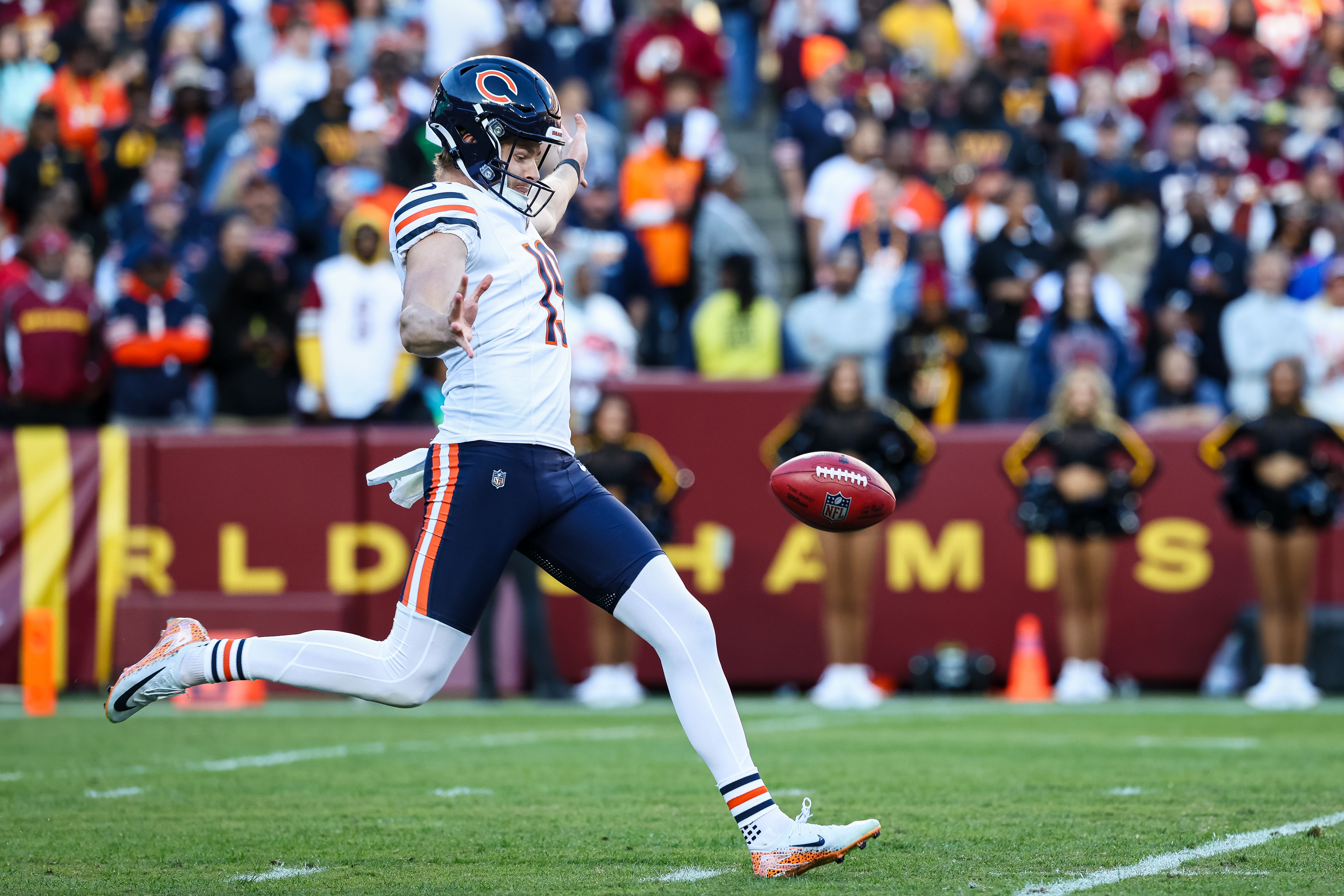Photo of a football player kicking a football in a game in a stadium. 