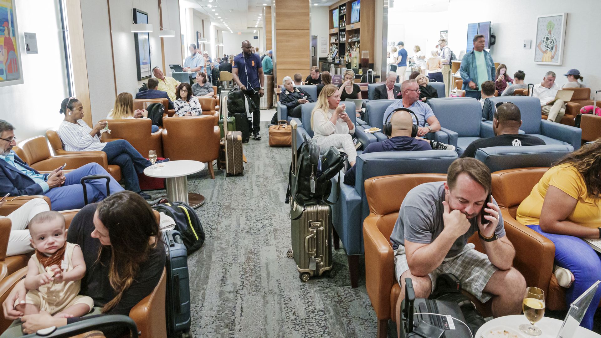 A crowded airport lounge with blue and orange chairs.