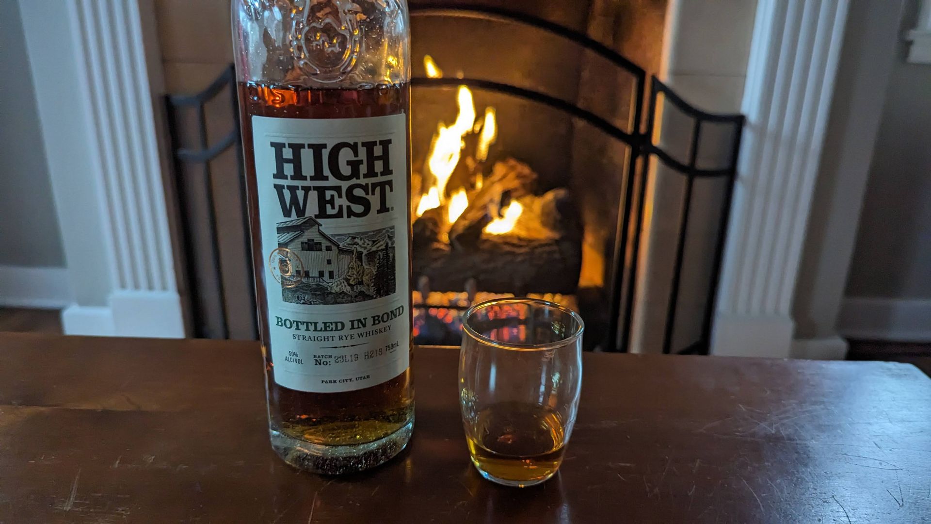 A bottle of whiskey and a glass of whiskey on a table in front of a fireplace.