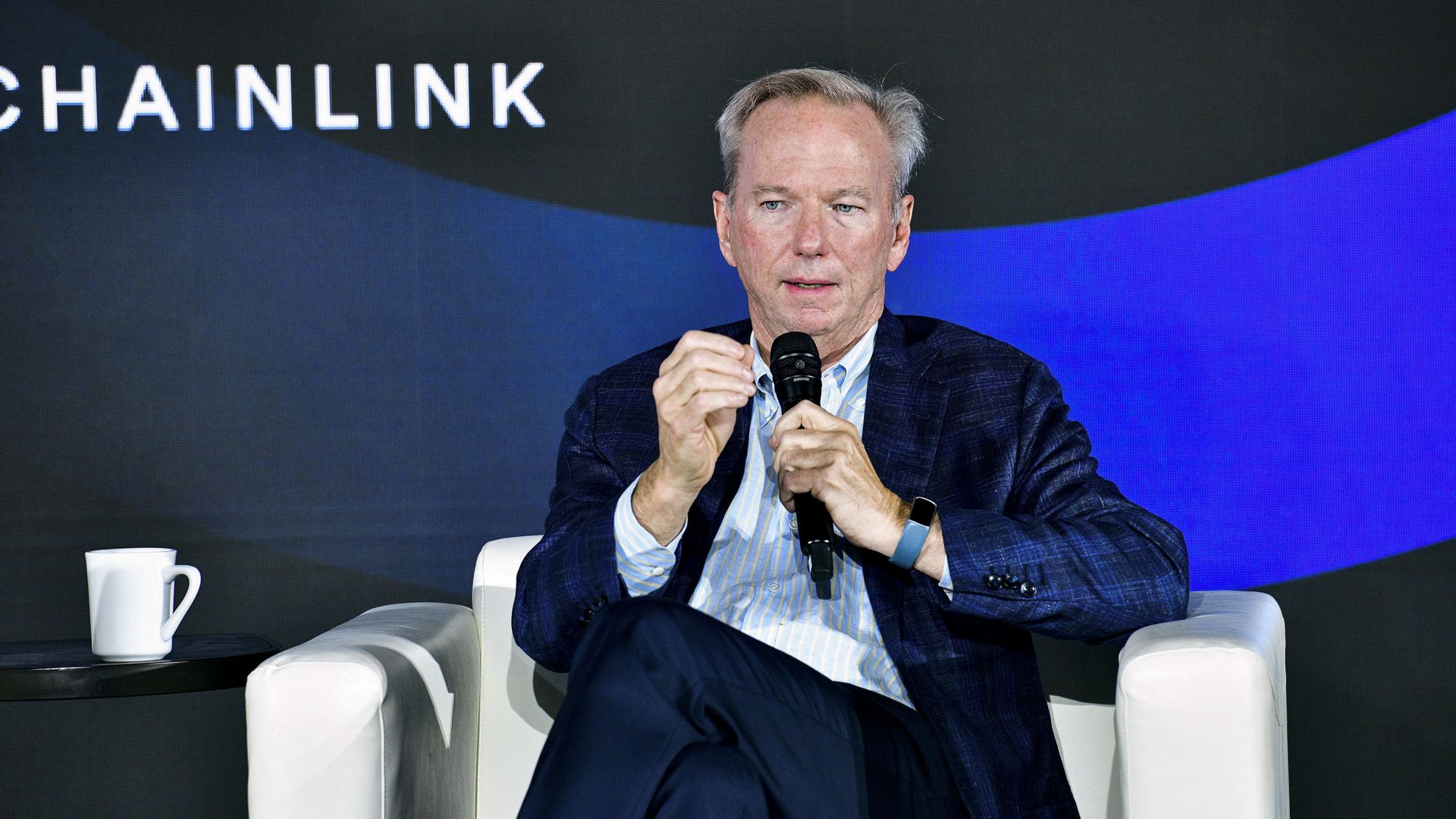 Former CEO & Chairman of Google Eric Schmidt speaks into a microphone while sitting in a chair