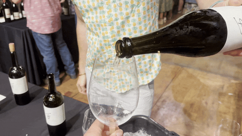 A person partially fills a glass of wine.