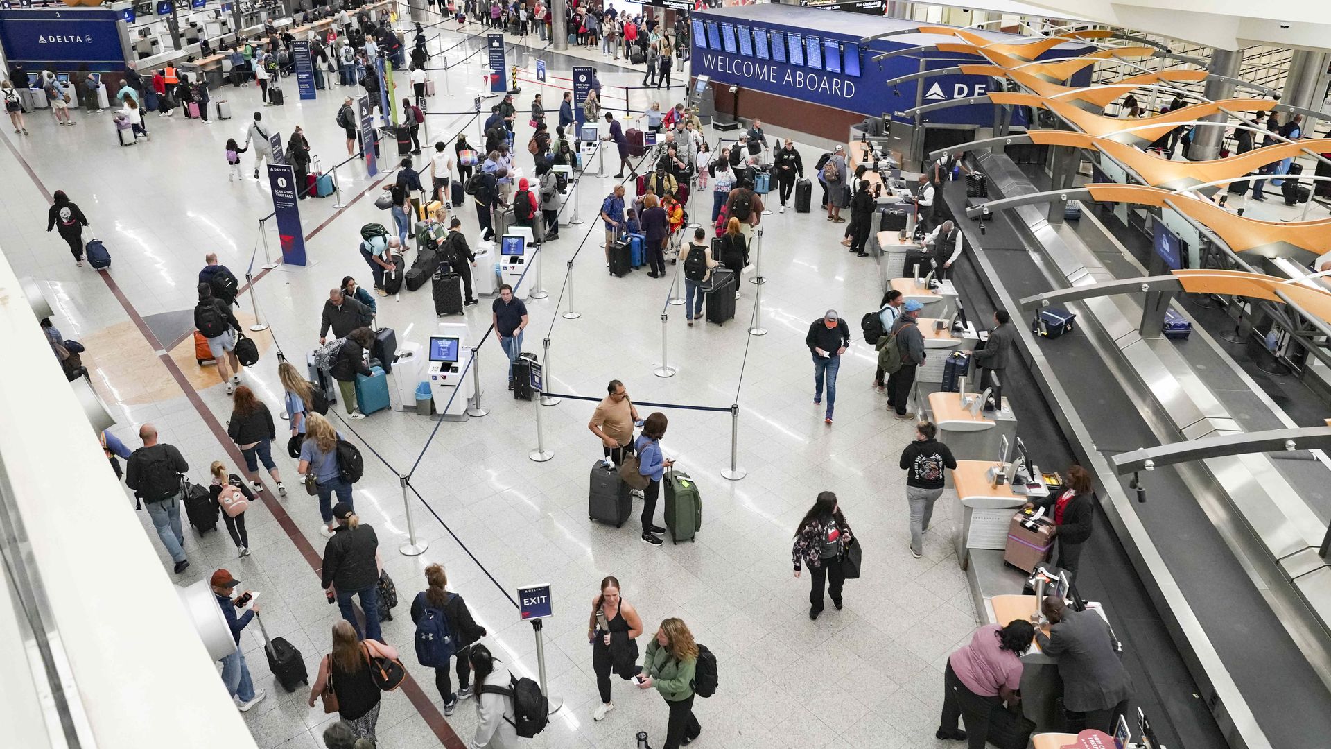 An overhead shot of people with luggage lined up waiting to check in at the Delta counter at an airport.
