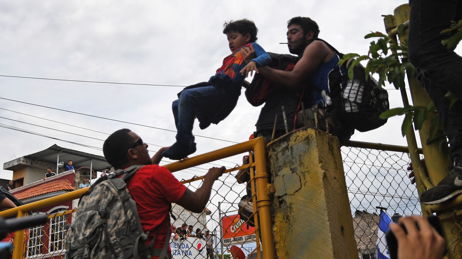 Honduran migrants lift a child over a gate