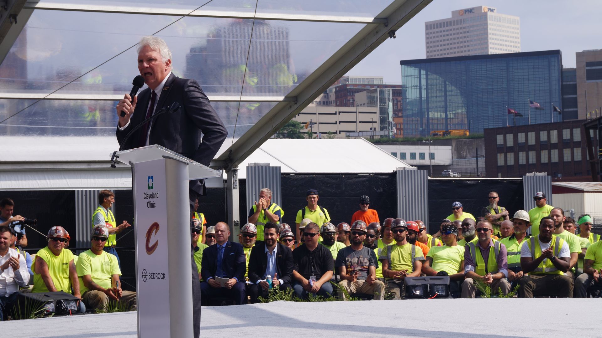 White man with mic in front of yellow shirted tradespeople
