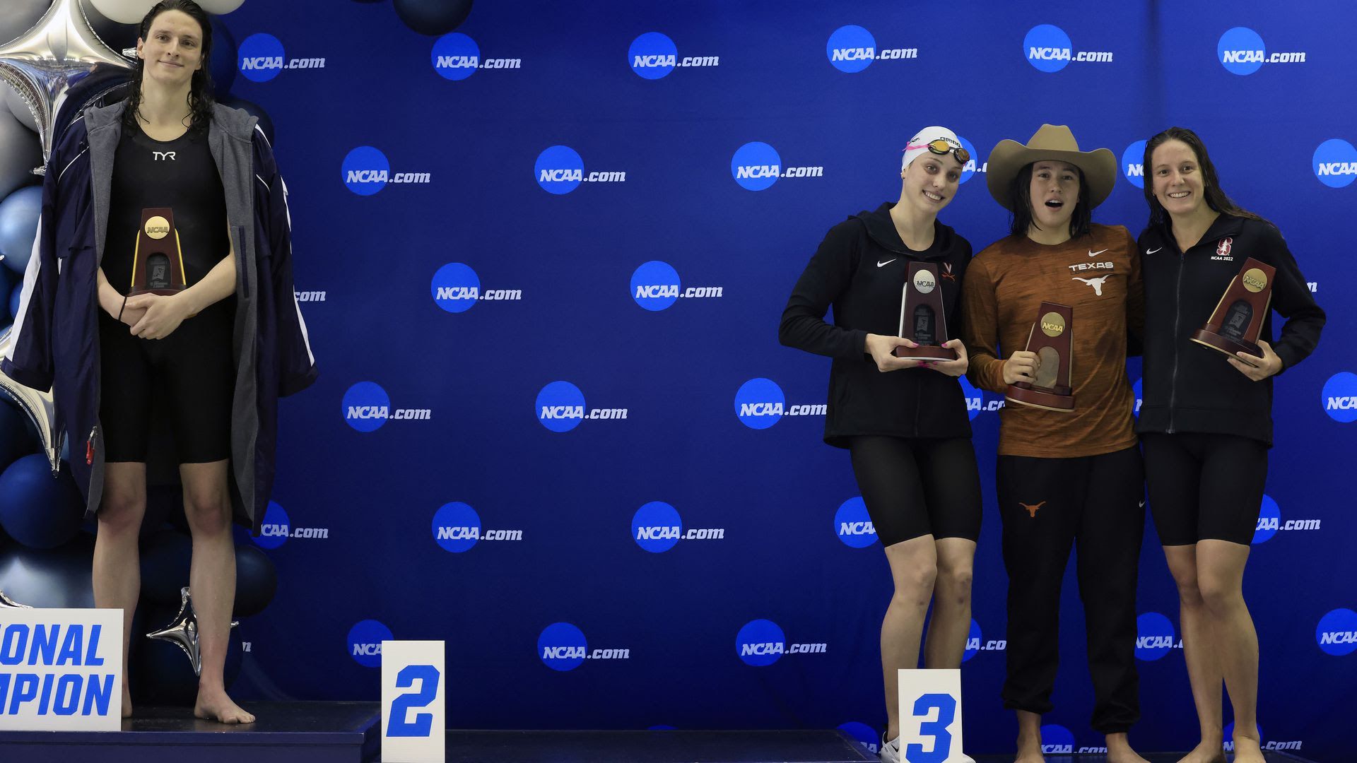 A photograph of University of Pennsylvania swimmer Lia Thomas standing on the podium after winning the 500-yard freestyle at the NCAA Division 1 Championships, as other medalists pose for a photo.