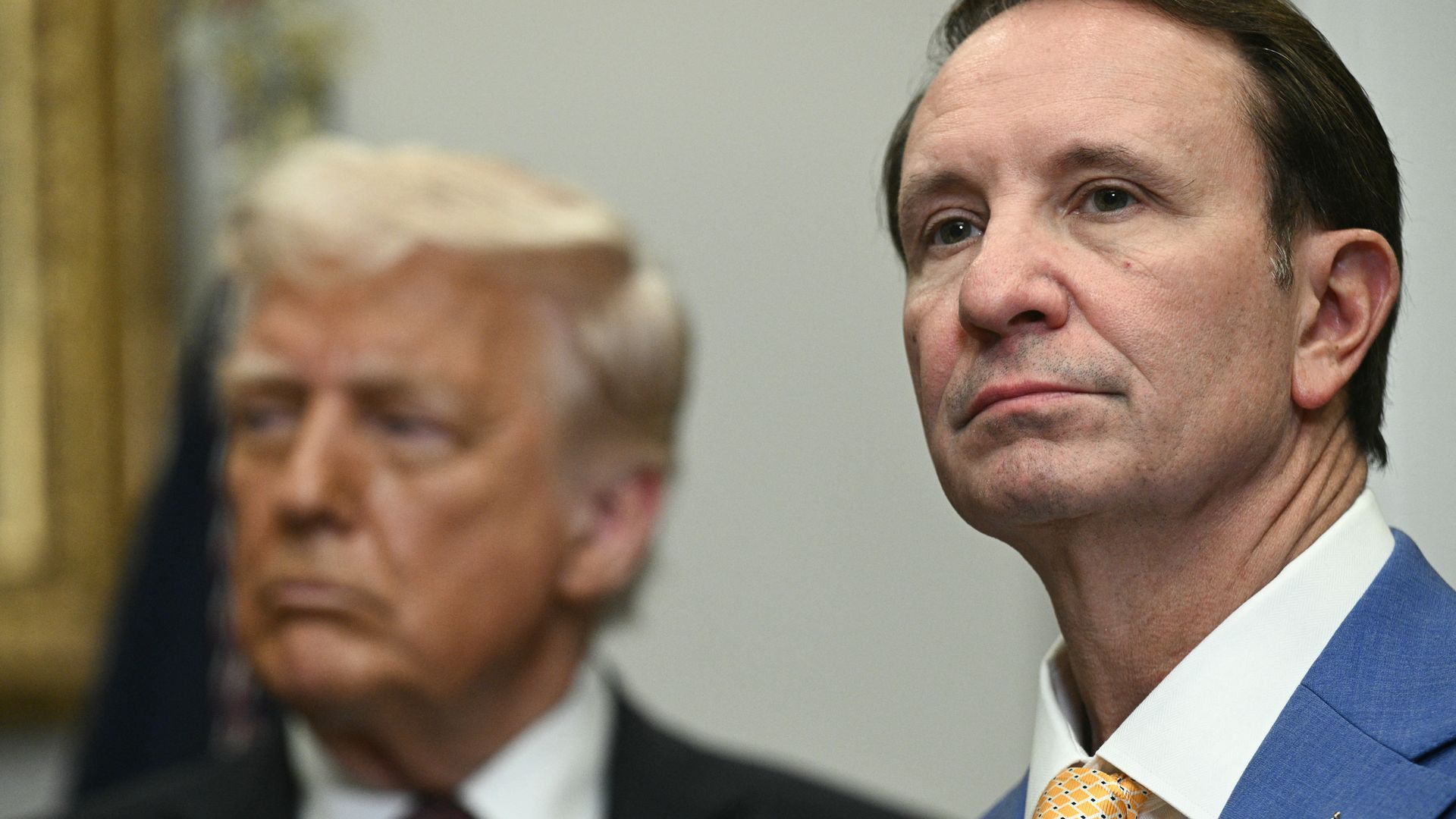 A close-up photo of Gov. Jeff Landry, with President Trump slightly out of focus behind him.