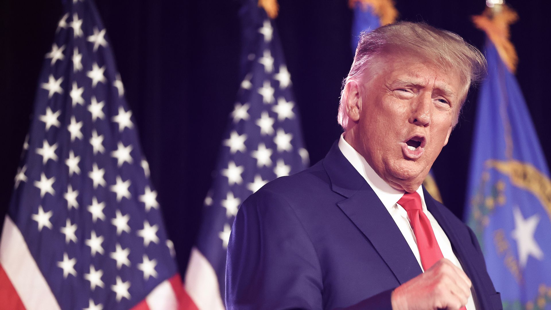 Photo shows Donald Trump gesturing on stage with flags in the background