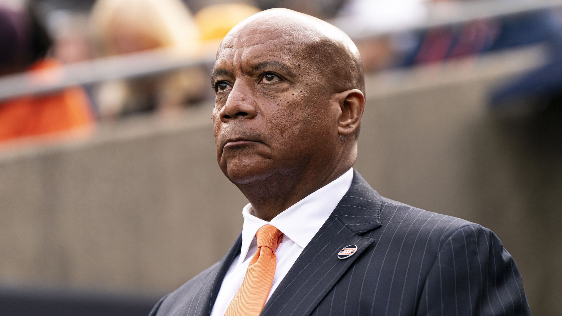 Photo of a man in a suit watching a game at a football stadium
