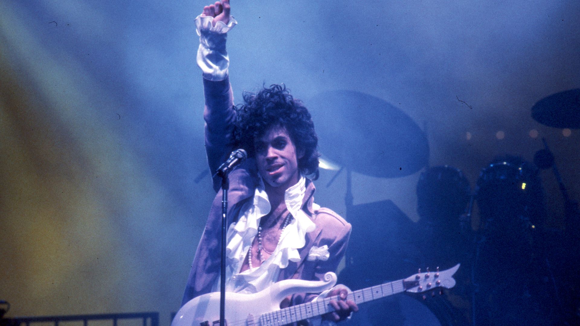 Price holds up his first while playing the guitar in a hazy room 