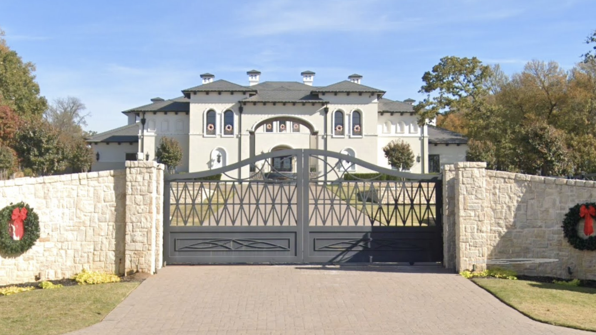 a white house behind a gray gate with wreaths on either side