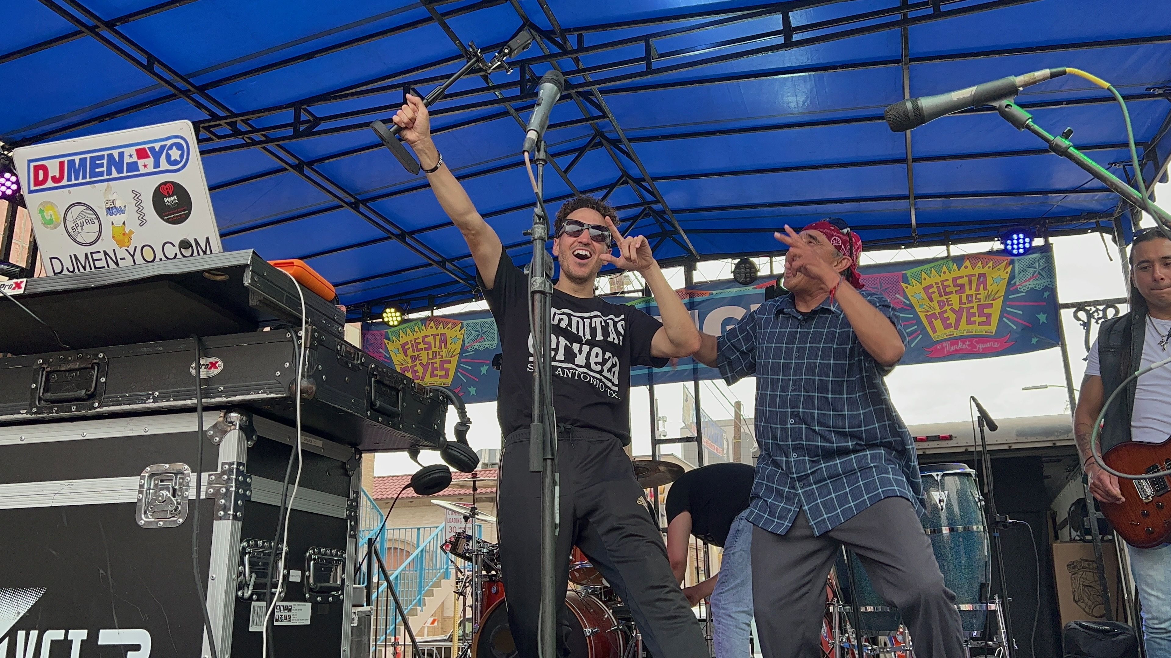 Two men stand on a stage with their arms up in celebration. 