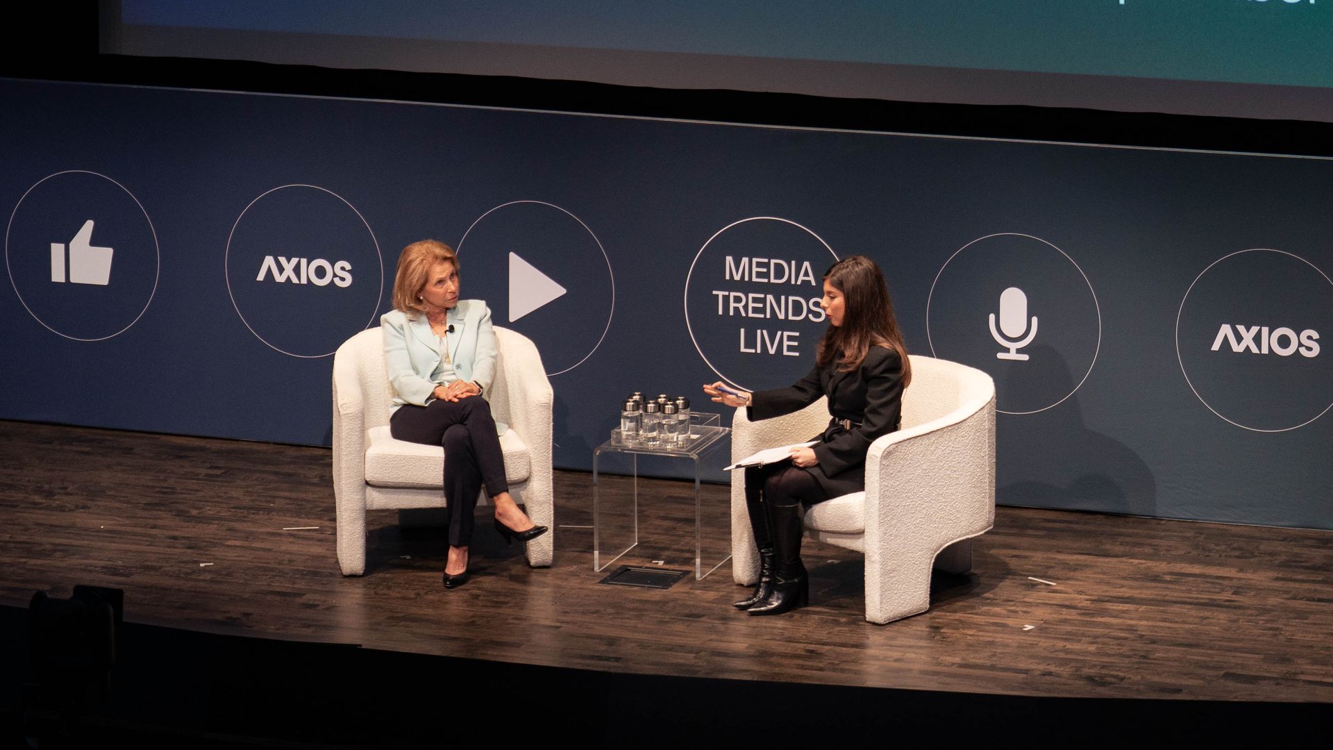 Two women seated on stage at Axios Live's Media Trends Live event in New York, with a large blue-green screen behind displaying event details and sponsors on September 18, 2025.