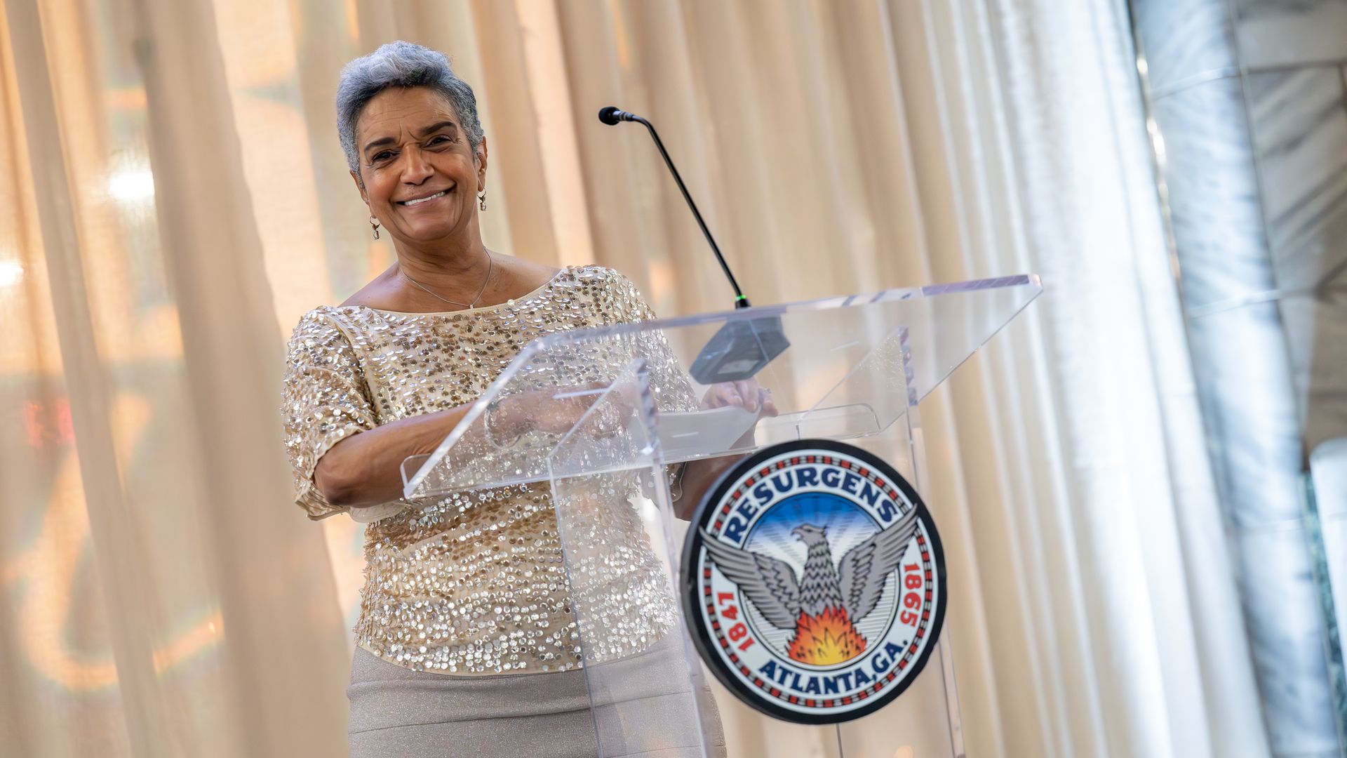 A woman smiles and stands at a transparent lectern with a City of Atlanta official seal