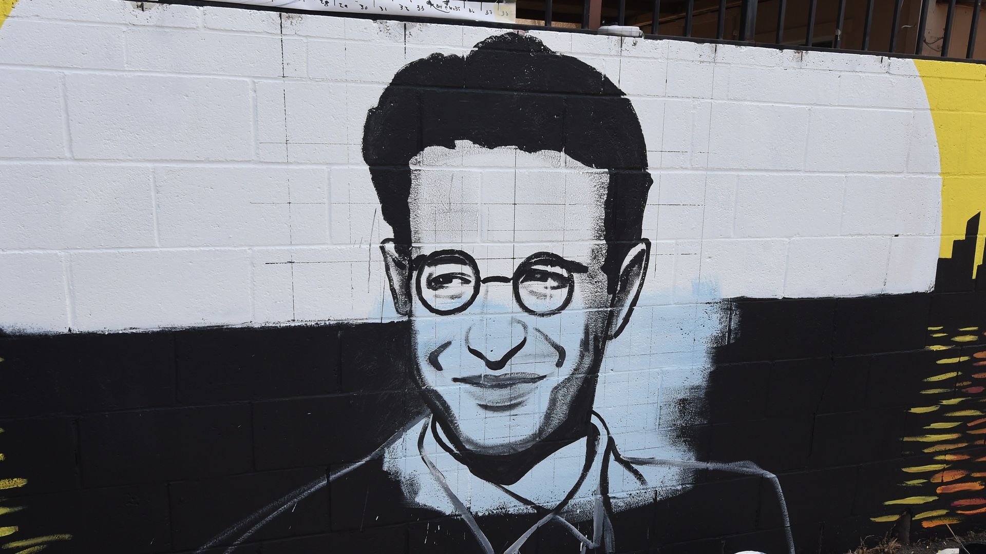 Picture of a mural painting of Daniel Pearl, he's seen wearing glasses and smiling. 